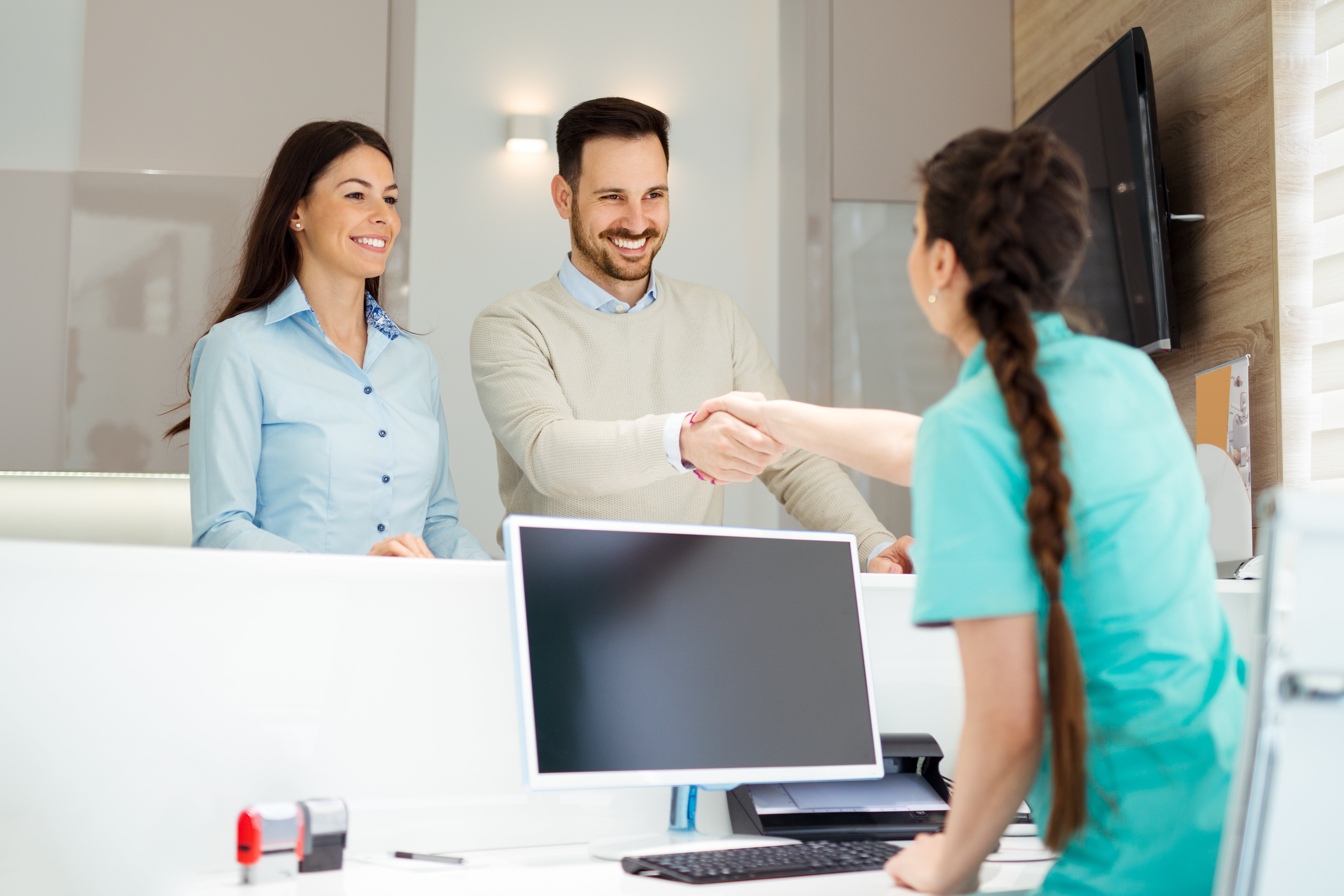 A couple at a dental clinic shaking hands with the dentist while checking out. 