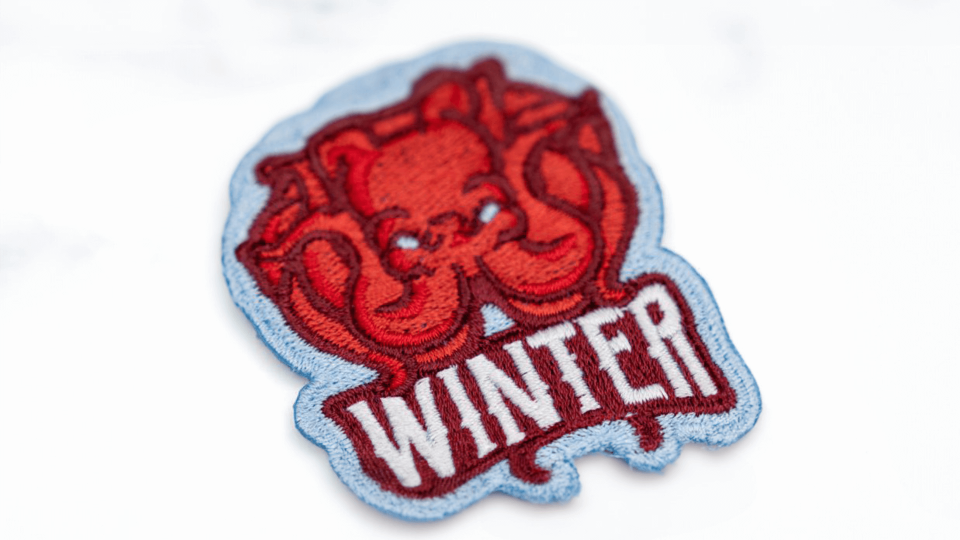 A red, embroidered winter-themed patch featuring a stylized bear with the word "WINTER" in bold white letters below it, surrounded by a light blue stitched border