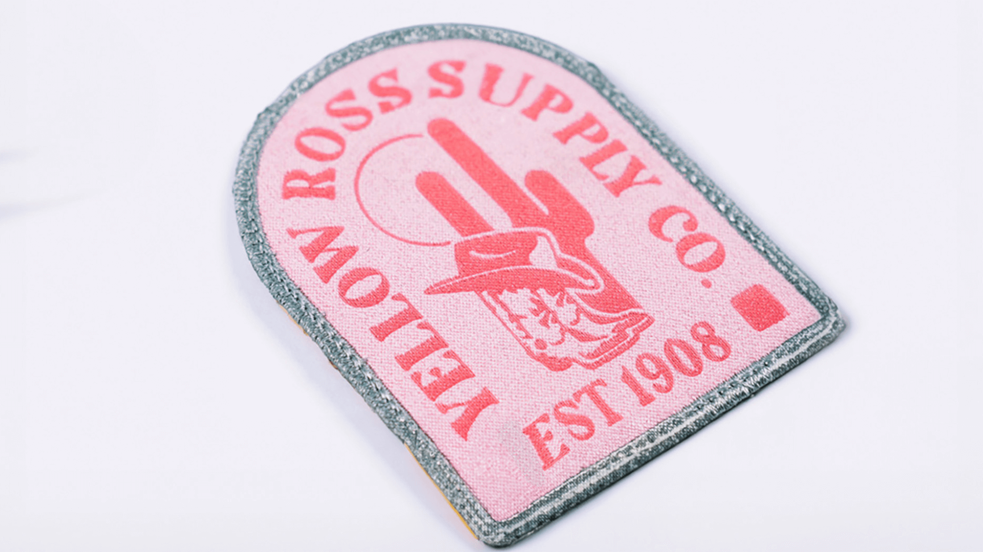 A vintage-style woven patch for "Yellow Ross Supply Co." in a pink and gray color scheme. It includes the text "Est 1908" with a design of a cowboy hat and cactus in the center