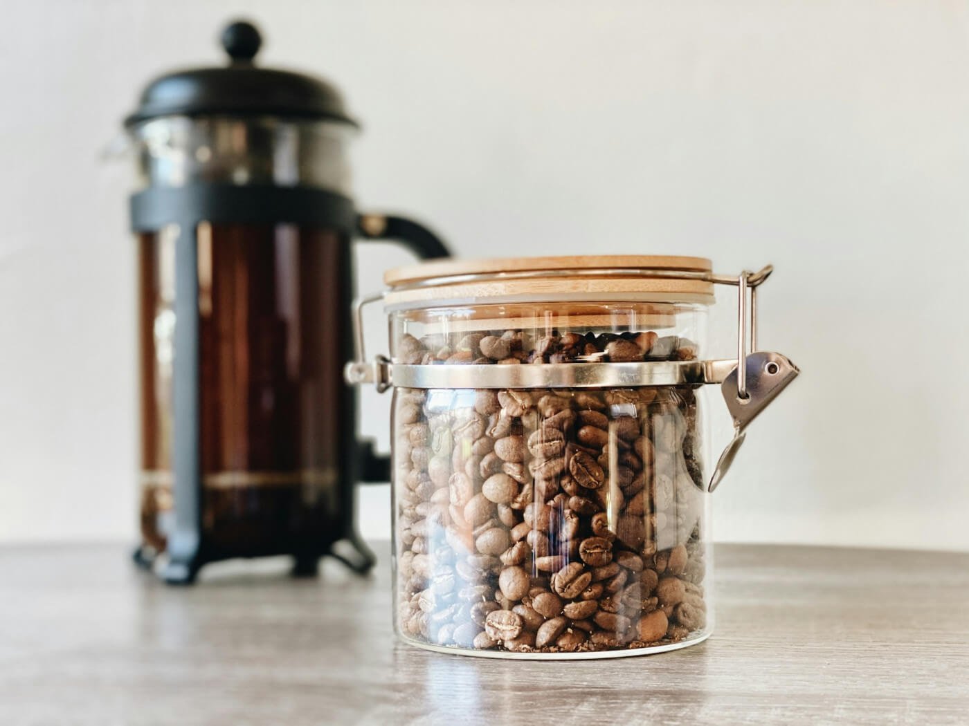 Glass jar filled with coffee beans next to a French press