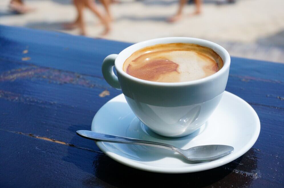 white cup of coffee on saucer with spoon on table