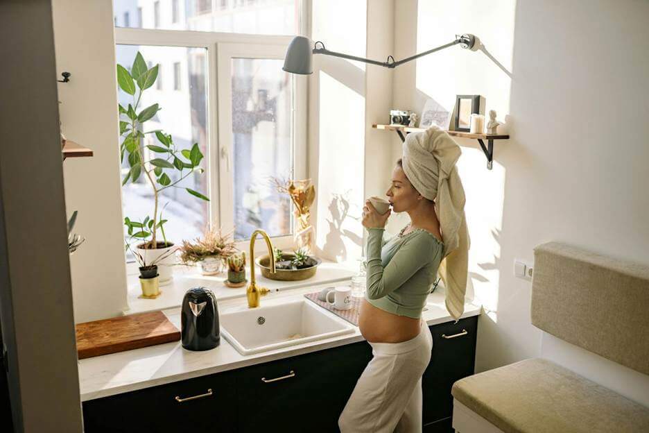pregnant woman sipping hot coffee near sink