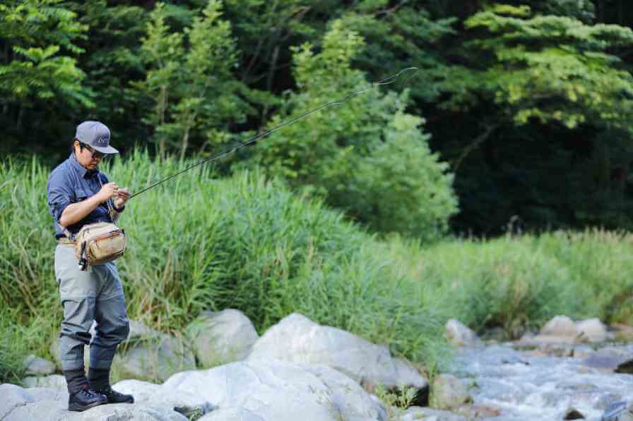 Fisherman tying a fishing hook while standing by a river