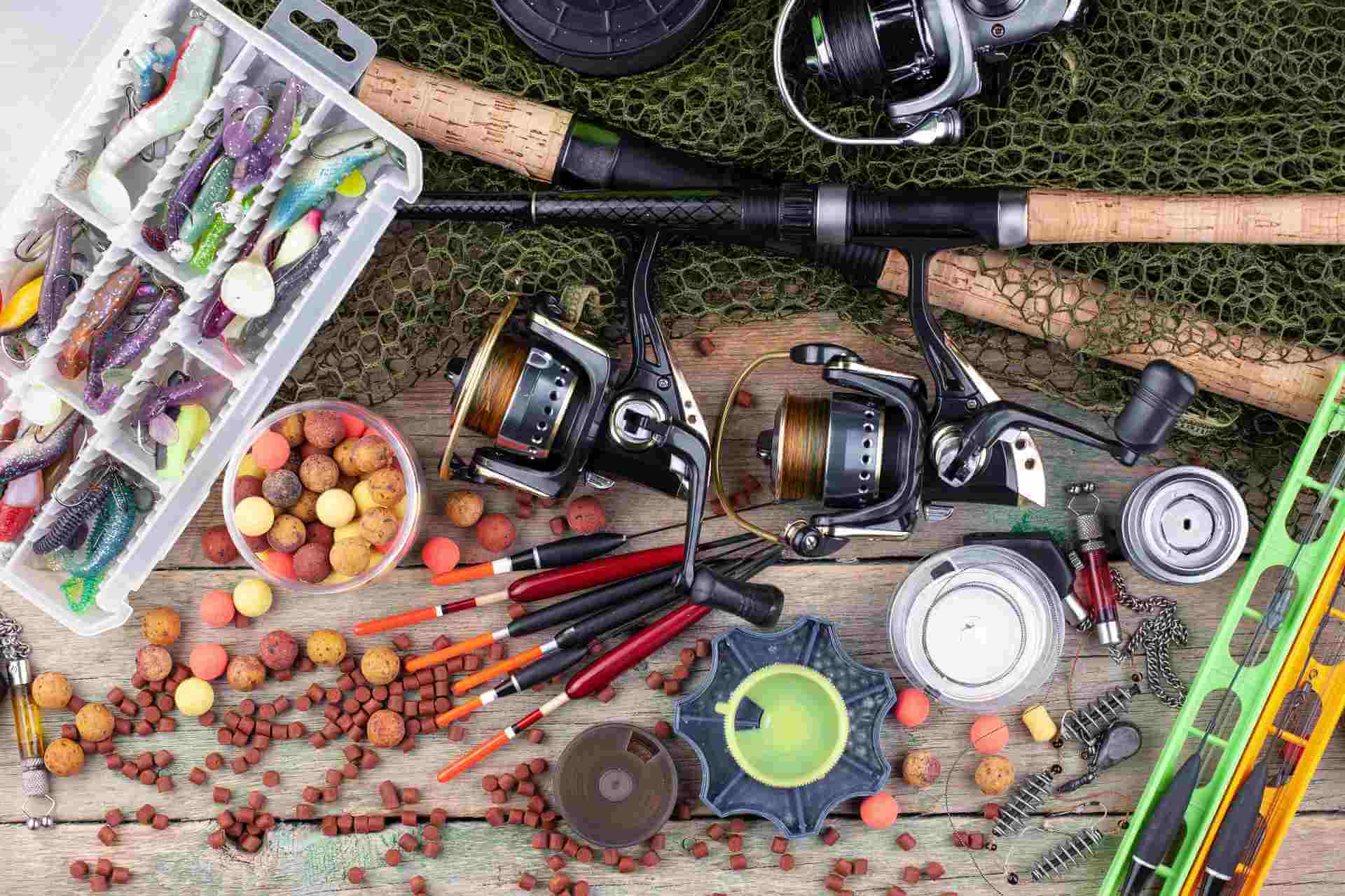 Various fishing tackle items, including lures, hooks, reels, and bait, spread out on a wooden surface.