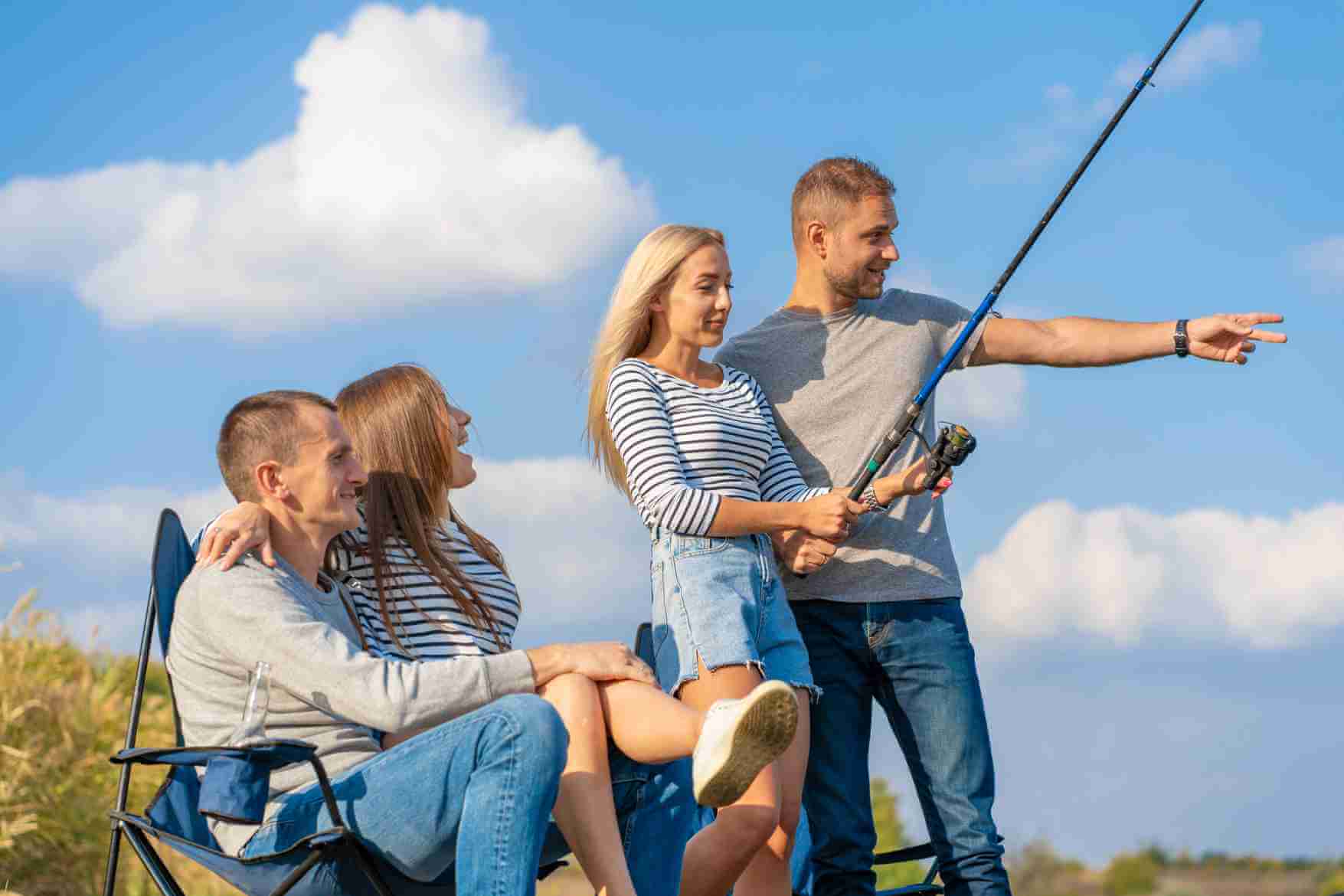Group of young friends fishing by a field under a bright blue sky