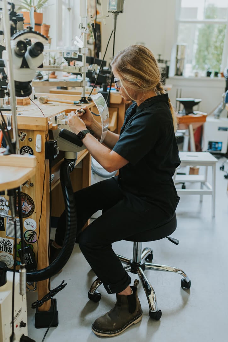 Jeweler, Corkie Bolton demonstrating essential safety tips by wearing safety glasses, hair tied back and no loose clothing using a flex shaft at a jeweler's bench.