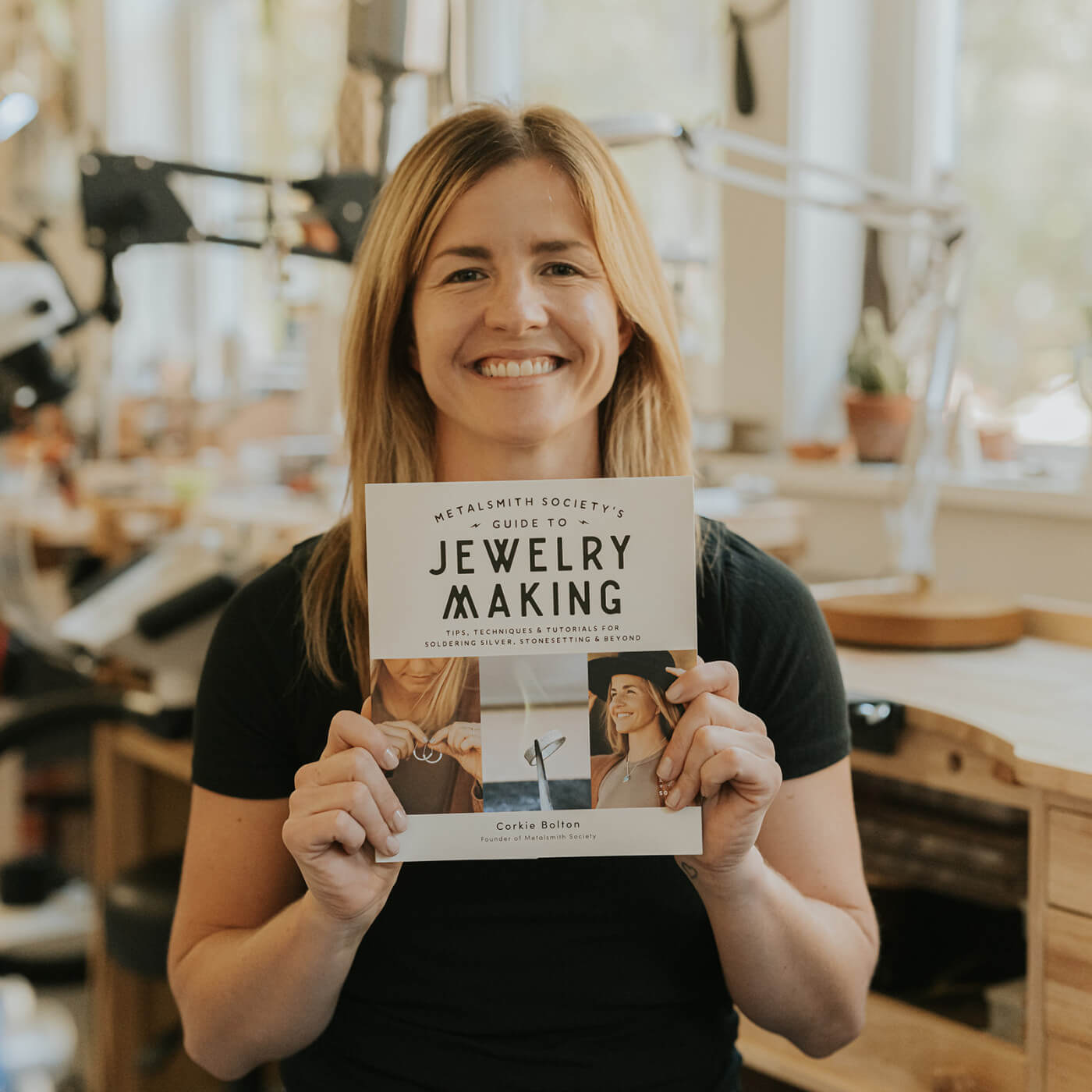 Corkie Bolton, author of Metalsmith Society's Guide to Jewelry Making, holding the book and smiling, showcasing the cover and sharing her passion for jewelry craftsmanship.