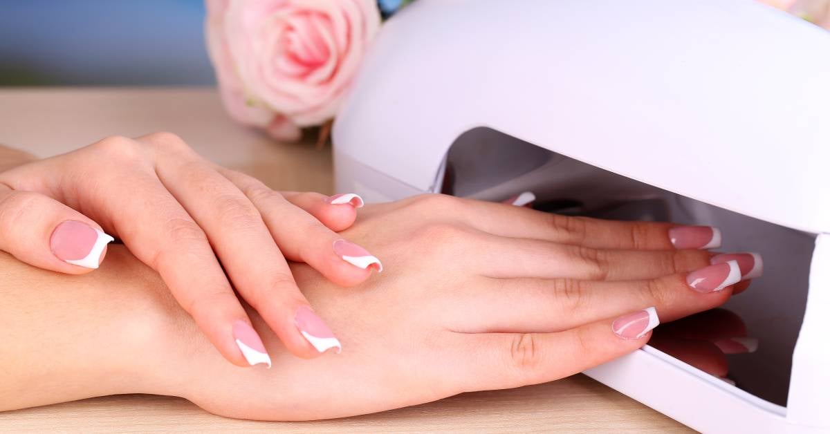 A close-up of a woman's hand showing off her French manicure, and they're under a lamp to help the gel dry.