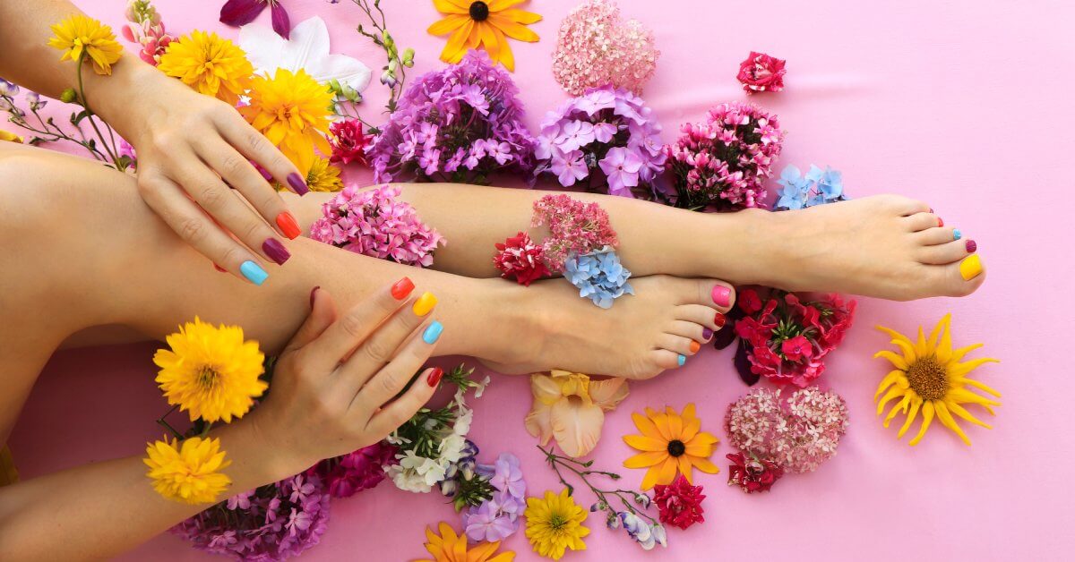 An overview of a multicolored manicure and pedicure on square-shaped nails. Different flowers surround the model.