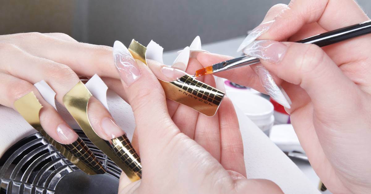 A close-up of a nail tech giving someone a manicure. The nail tech is using a French tip manicure tool for preciseness.