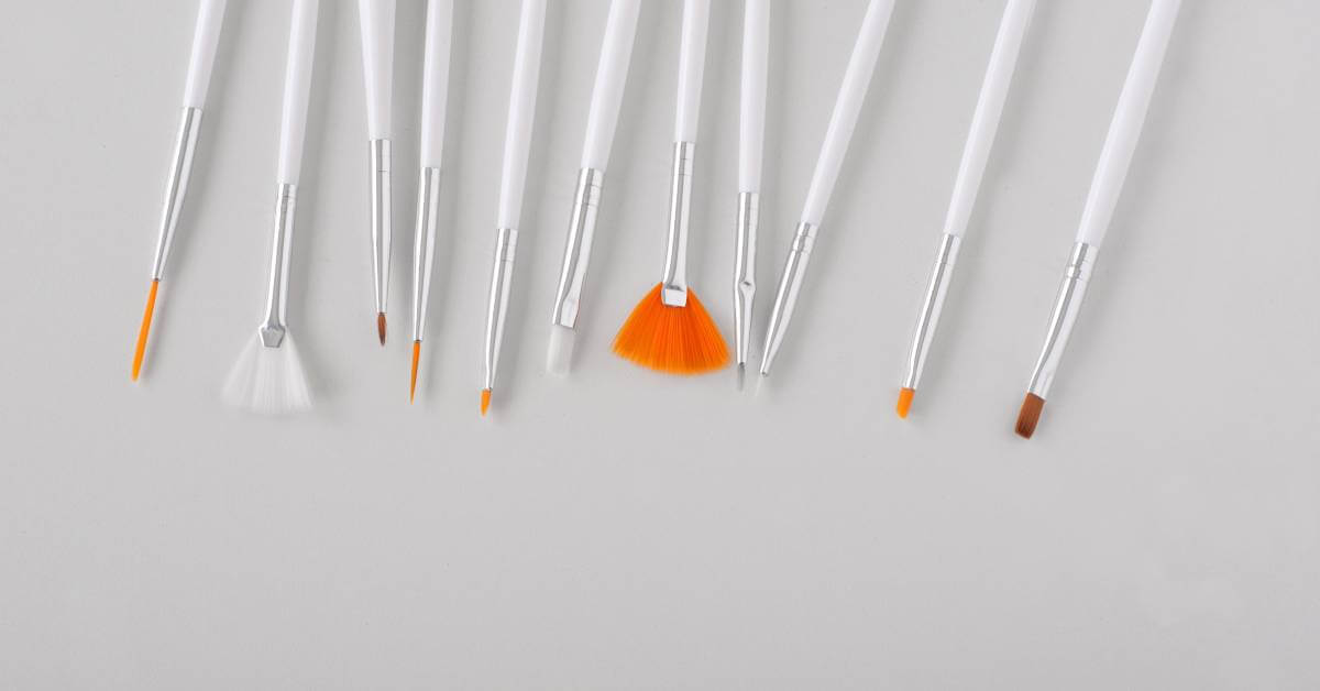 A set of 11 white nail art brushes lying beside one another, each with a different shape for varying designs.