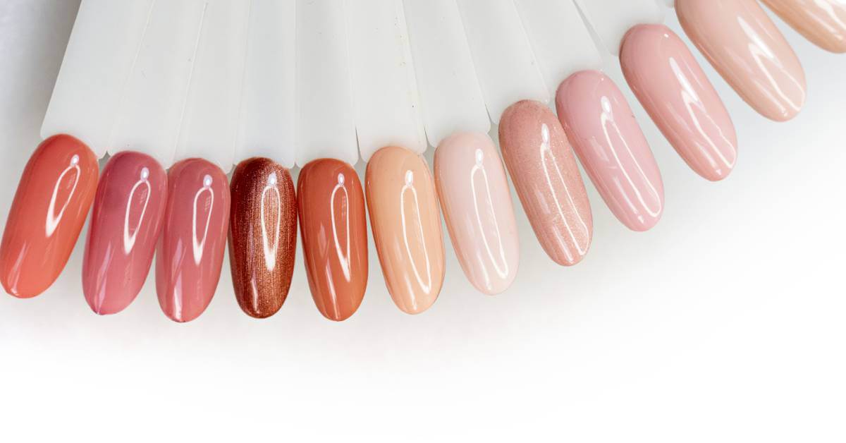 An array of almond-shaped, tester acrylic nail tips painted different shades of nude including cream, mocha, and pale pink.