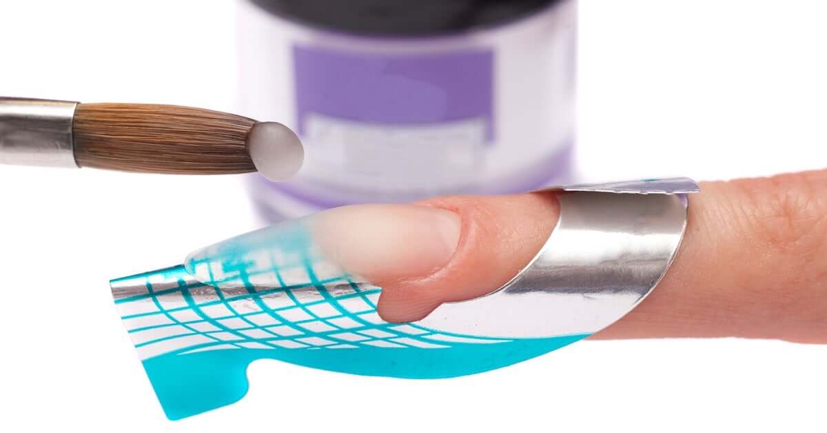 A technician applies a silver-and-blue extension form on a finger, prepping the acrylic overlay over the bare nail carefully.
