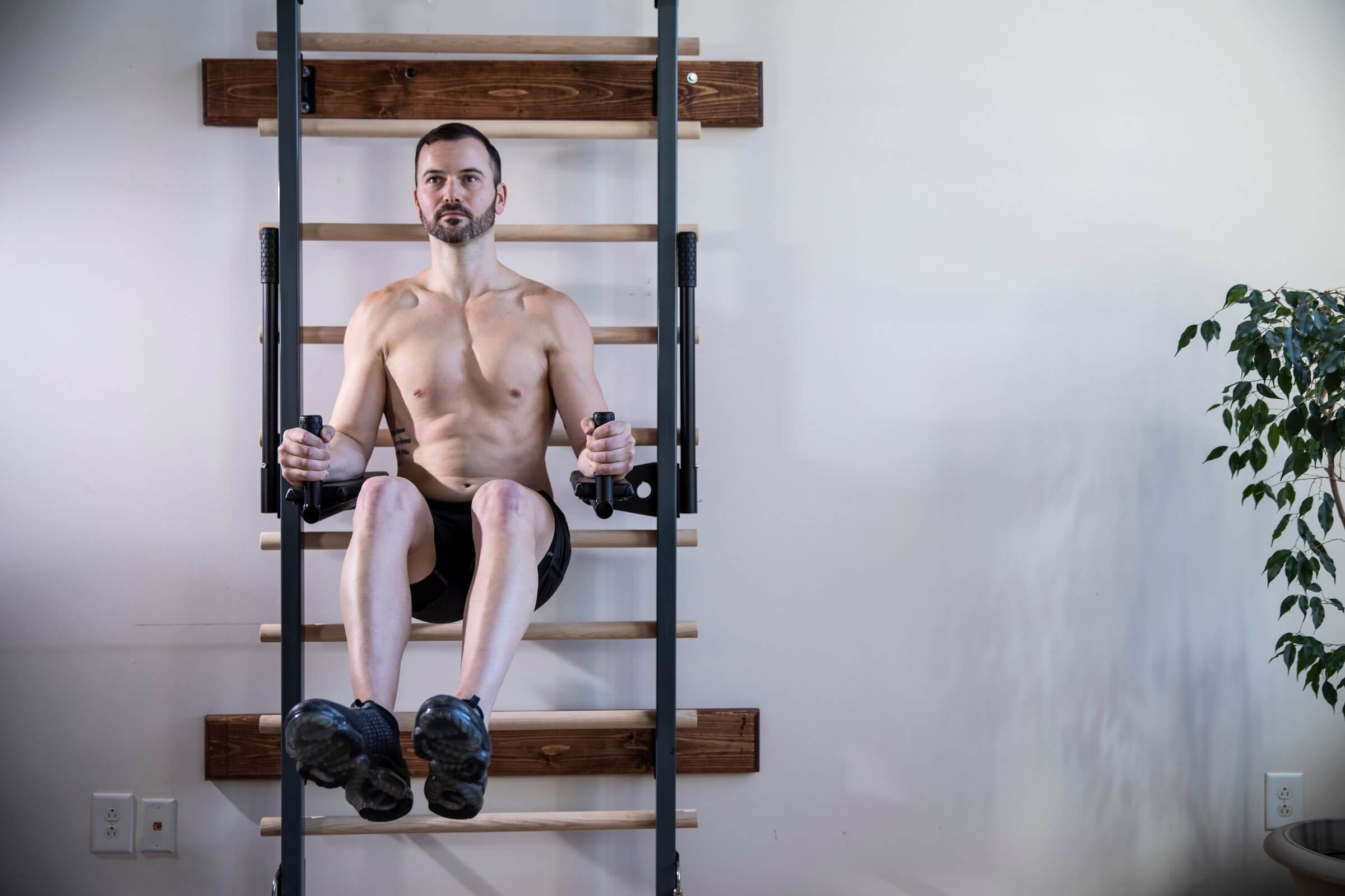 Man performing a barre workout using wall-mounted wooden barres, focusing on core strength and posture during an upper-body and balance exercise.