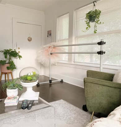 A bright, cozy living room featuring a ballet barre near a sunlit window, surrounded by plants and neutral decor—an inviting space for a home barre workout.