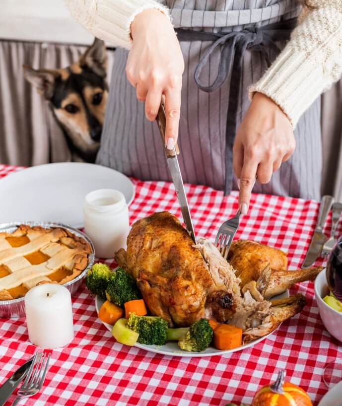A person cutting a turkey with a dog behind it