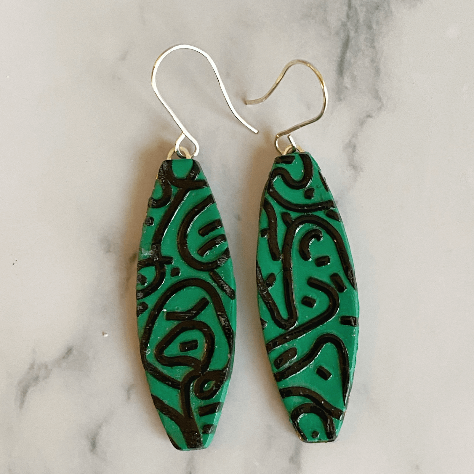 A pair of green polymer clay earrings with a black graffiti design.