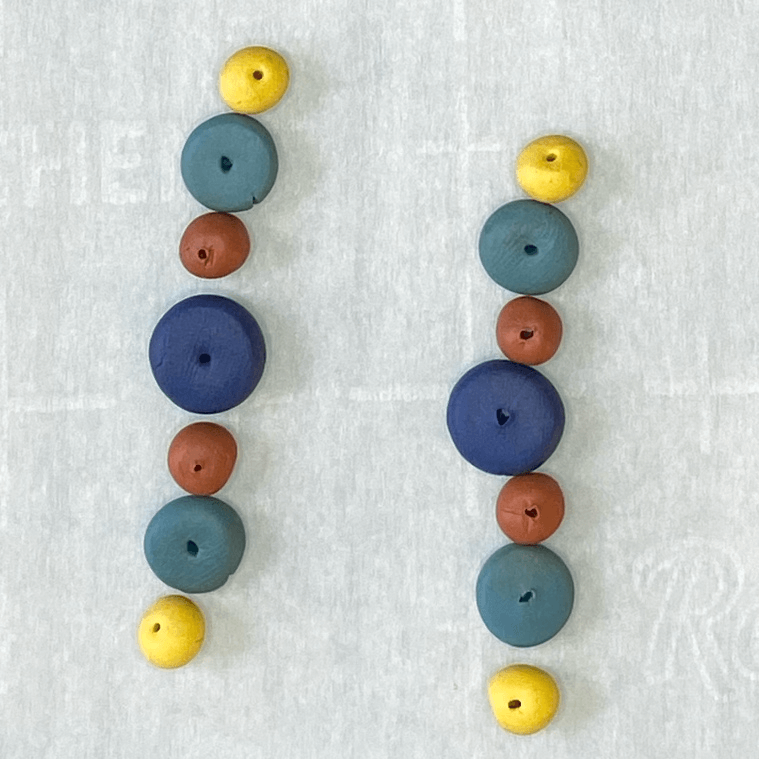 Baked polymer clay beads lined up in earring order.  Temperature flares in the oven darkened the clay color.