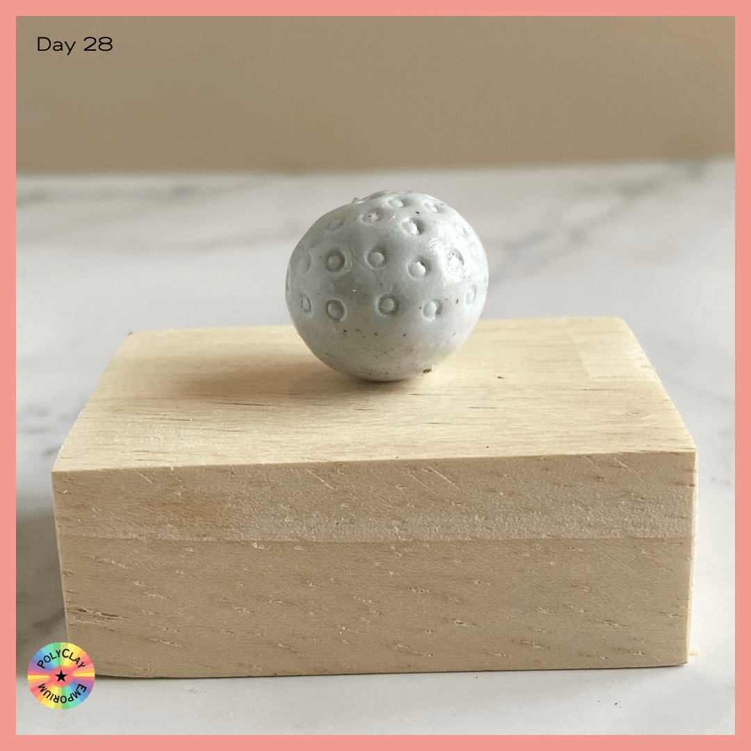Pale green polymer clay bead with circular indentations.