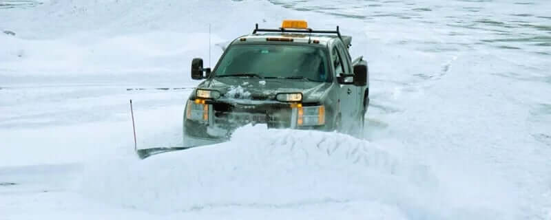 GMC Pickup truck fitted with a snowplow pushing large snow bank in a snowy parking lot.