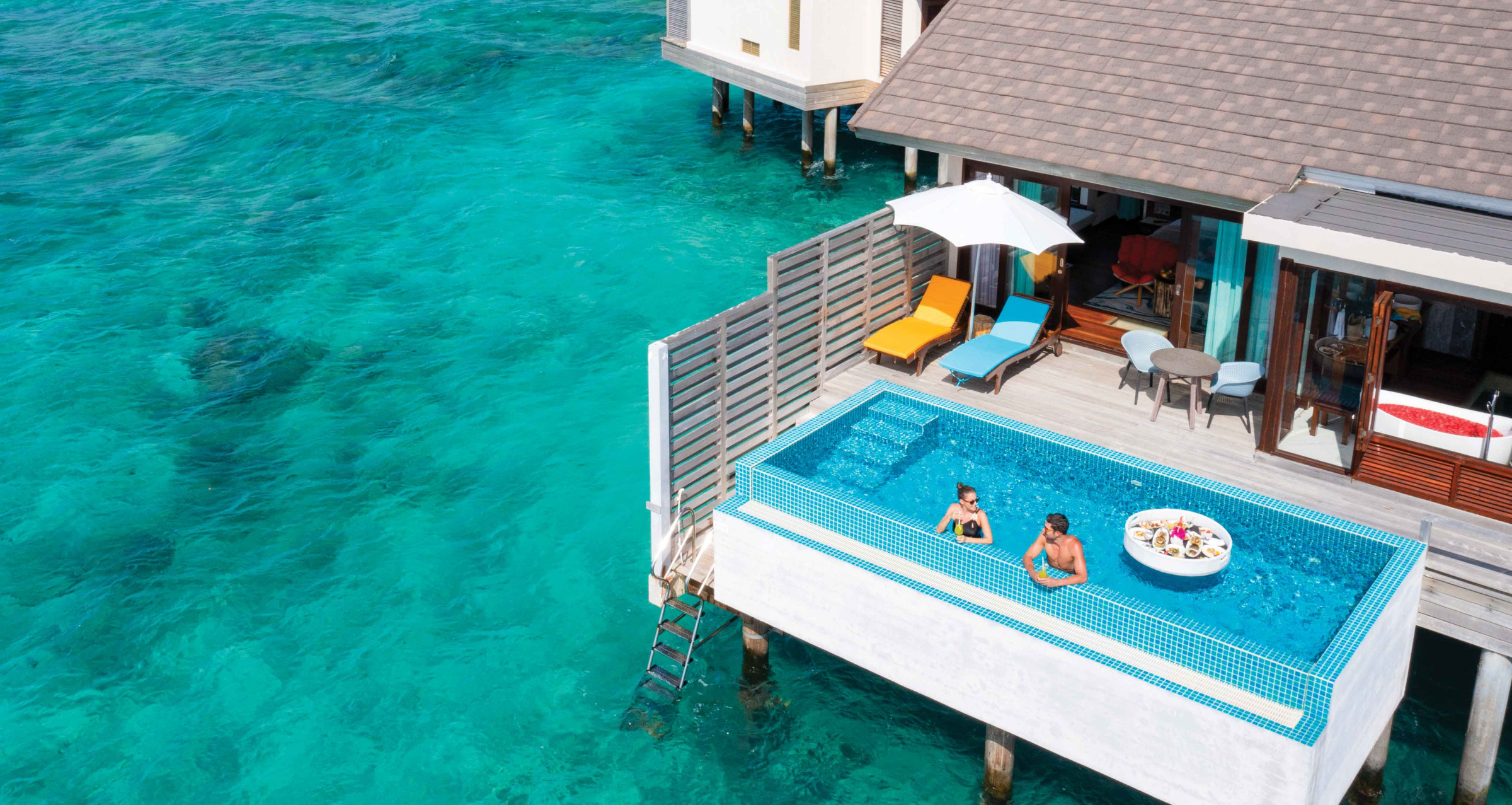 A couple enjoying a floating breakfast in the pool of their overwater villa at Atmosphere Kanifushi.