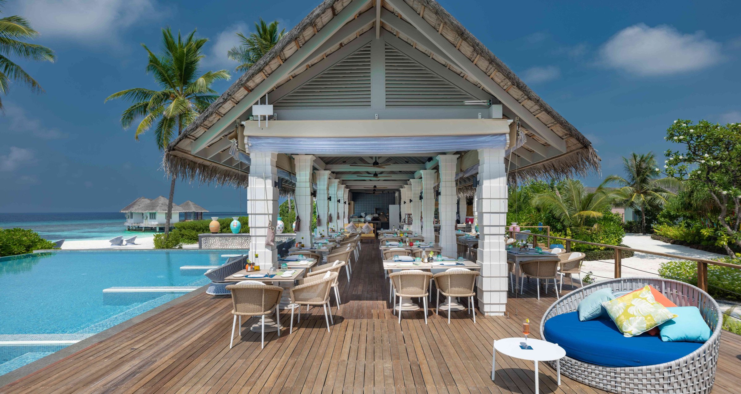 A shot of Acquapazza restaurant at Cora Cora Maldives, with some indoor seating, some outdoor seating on the deck bordering the pool and the beach.