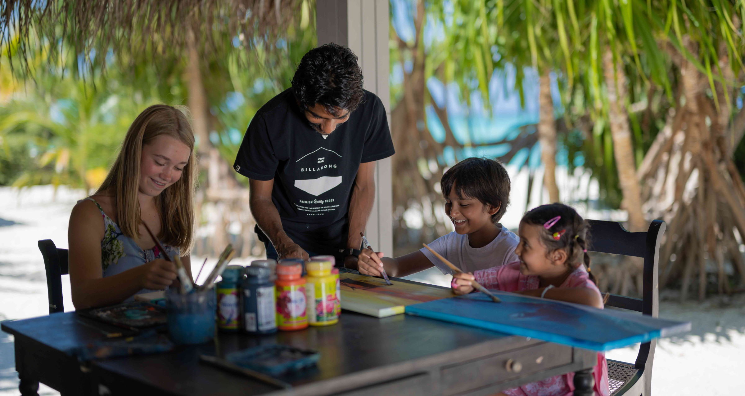 Three children taking part in a painting session with a member of staff at CoRa kids Club at Cora Cora Maldives.