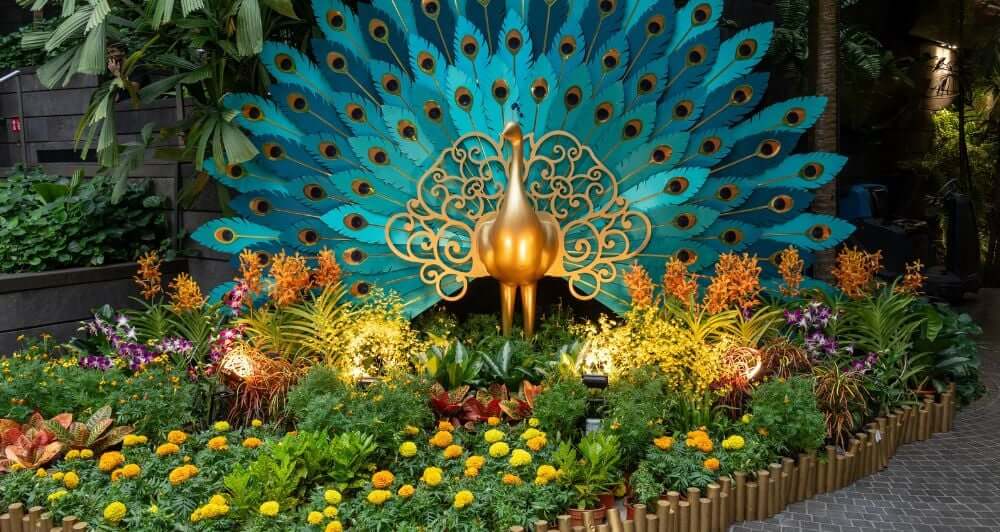 a golden and blue peacock statue in the middle of a patch of flowers