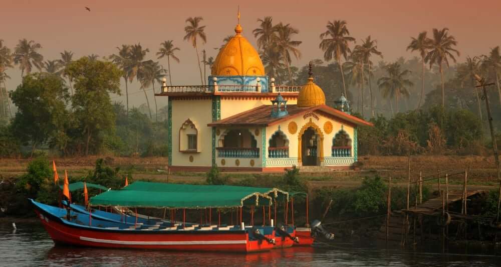 a temple in India, sat along side a river with river boats 