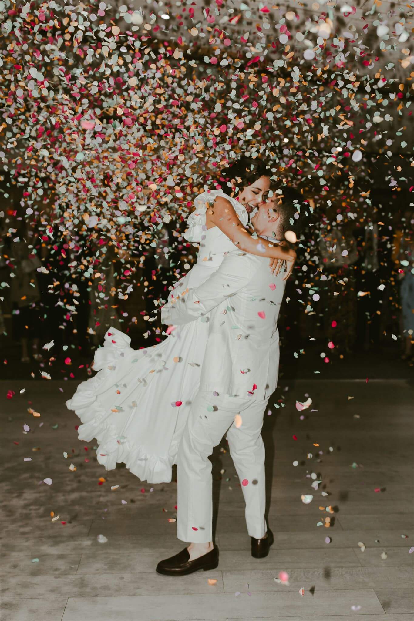 A groom lifts his bride into a shower of colourful wedding confetti