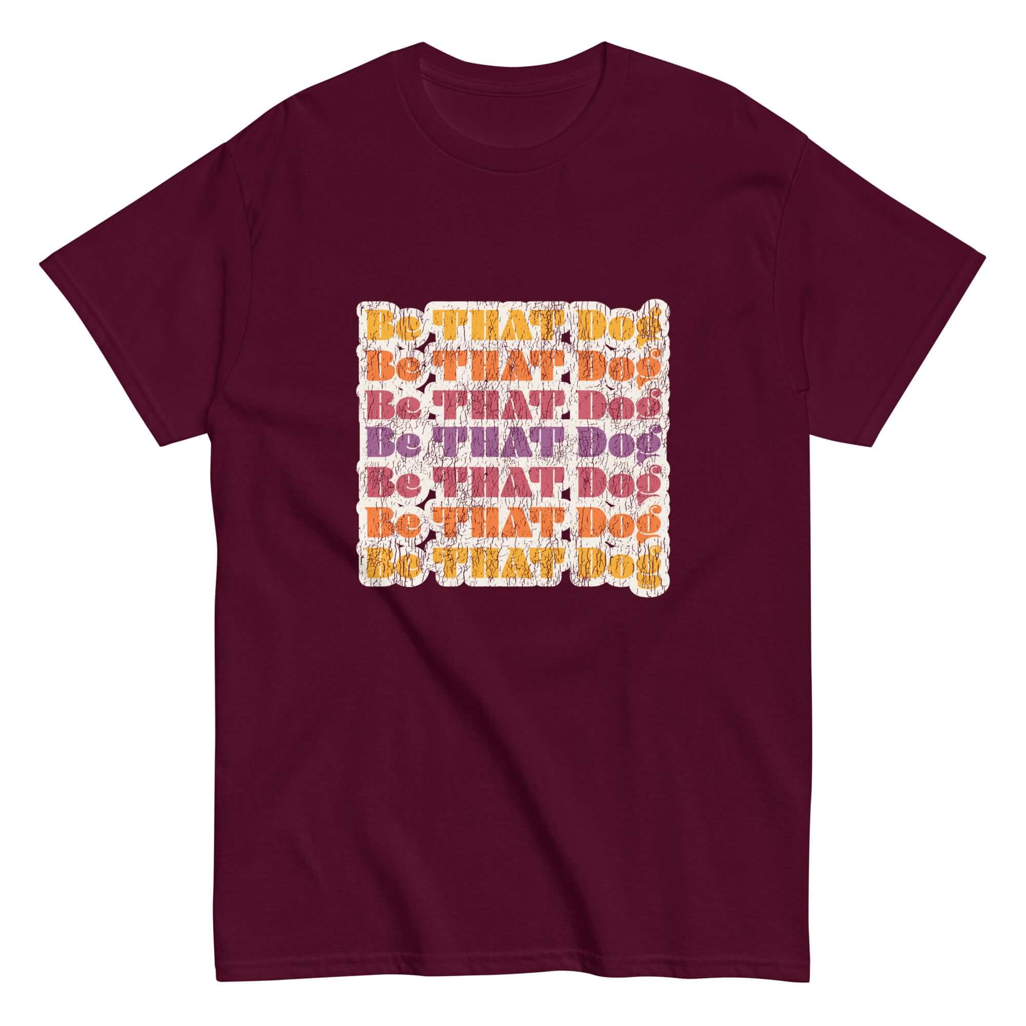 Unisex maroon t-shirt featuring a retro-inspired design with the repeated phrase 'Be THAT Dog' in a distressed font. The text alternates in vibrant shades of orange, purple, and white, creating a bold and playful look for dog lovers.