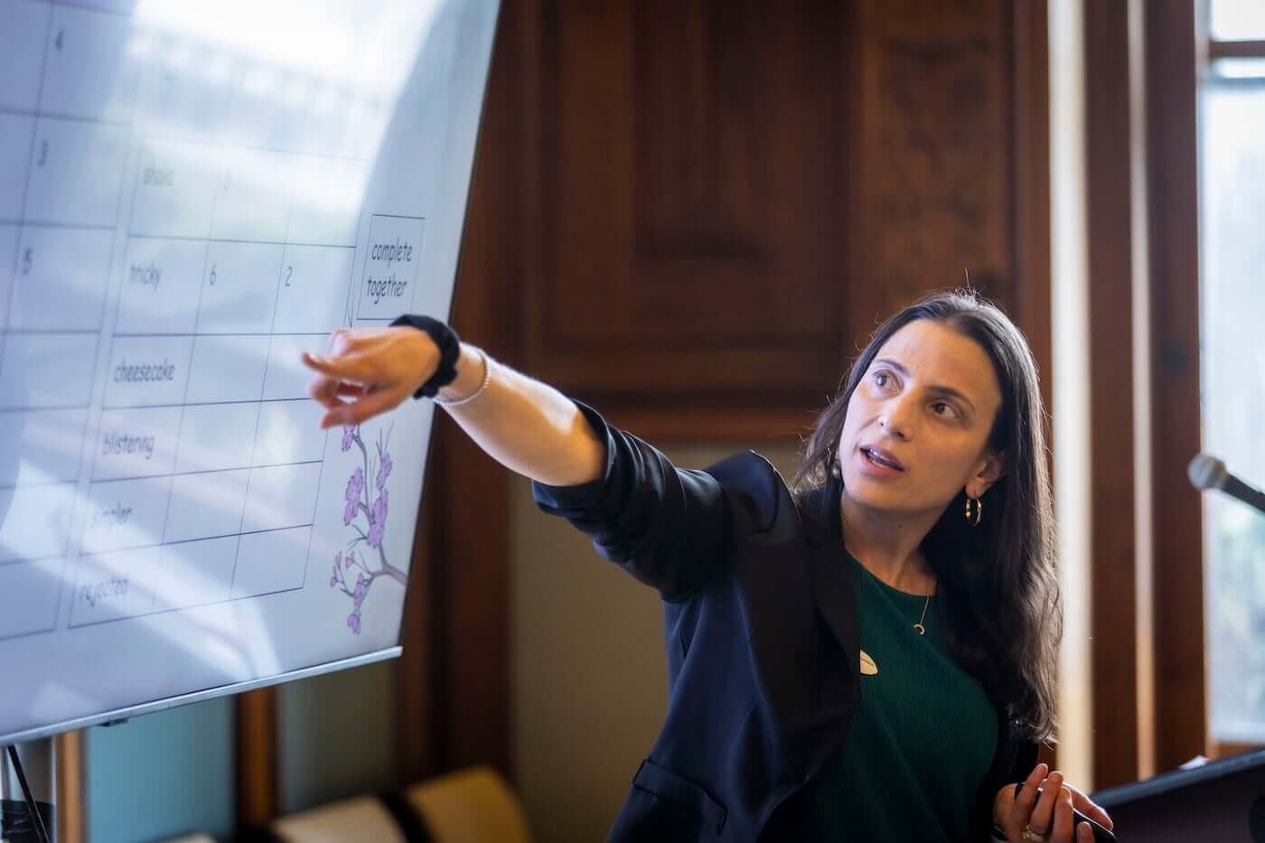 Speaker standing in front of presentation on screen and pointing at data