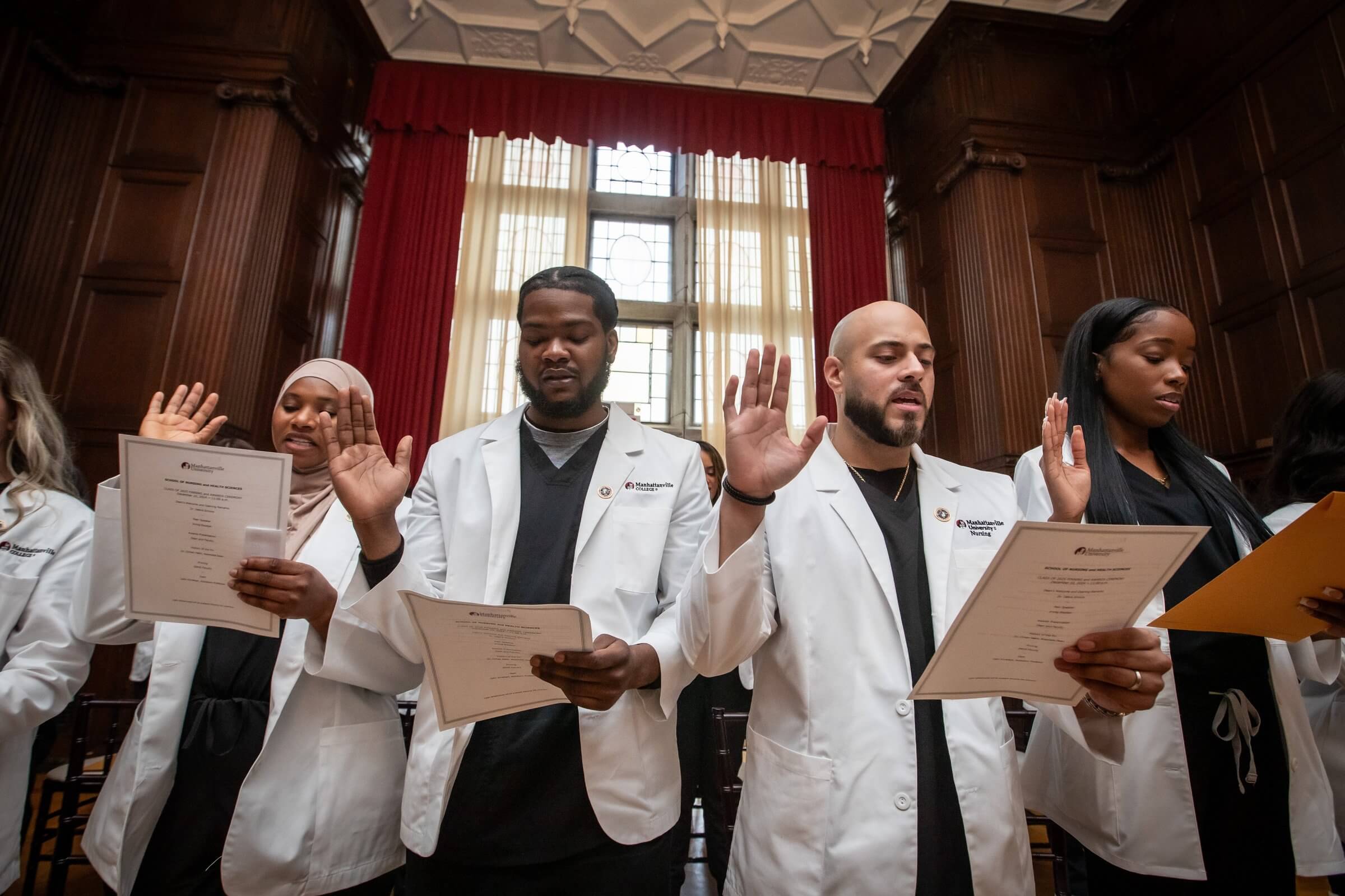 Nursing students in white coats holding up their right hands and taking oath