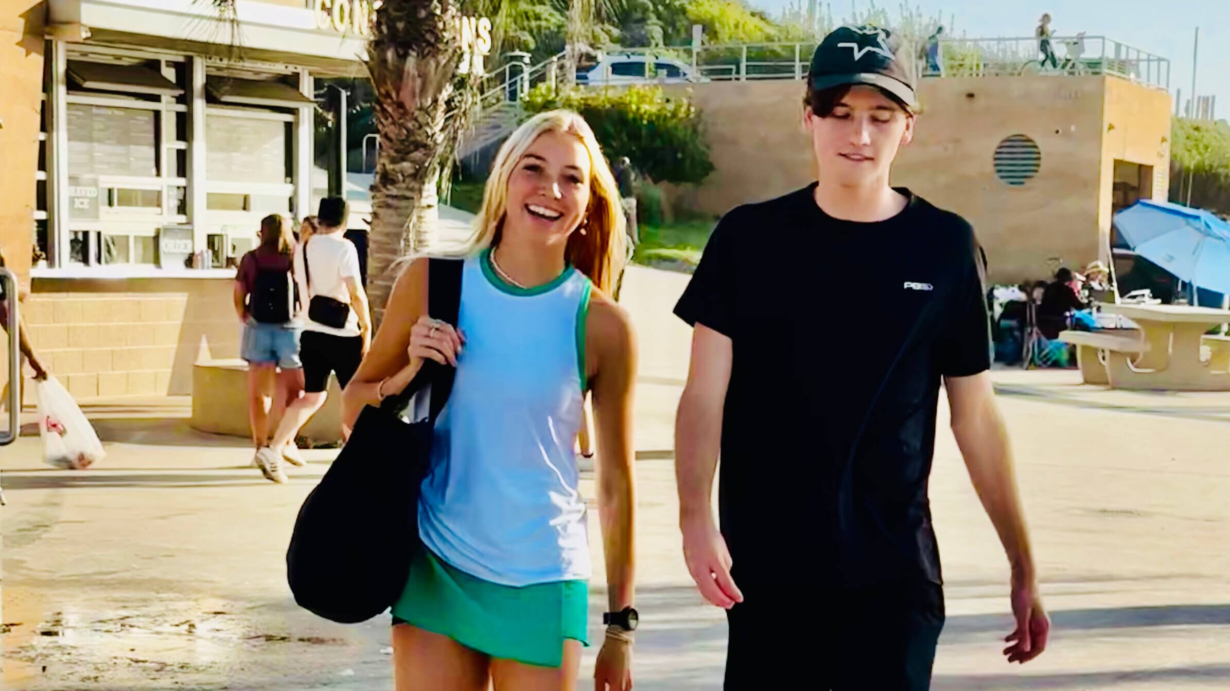 Two students who are college-aged walking while wearing and carrying some pickleball gear.