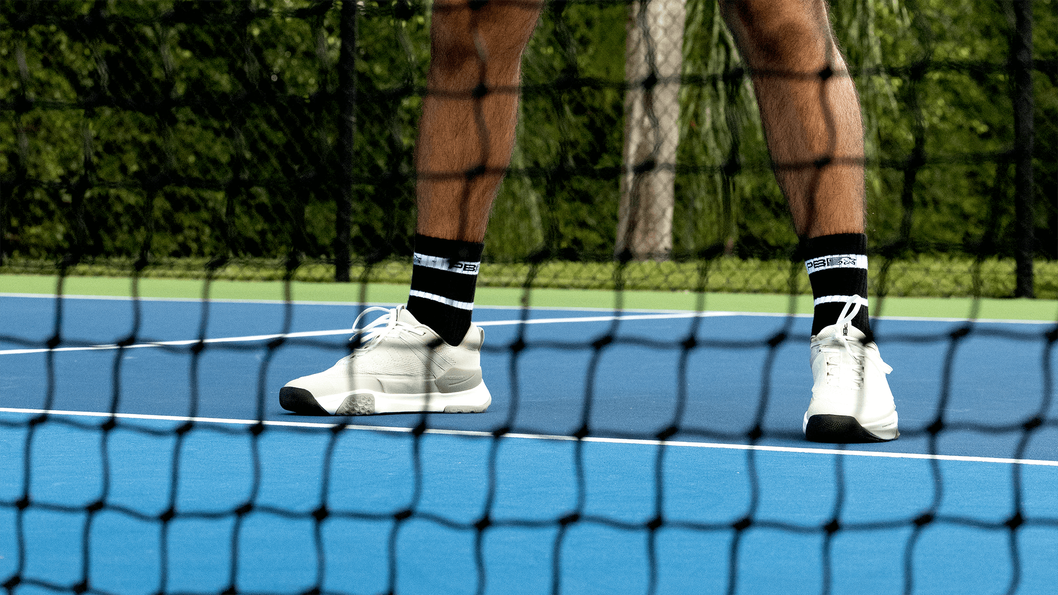 Close up of a pickleball net and two feet on the court