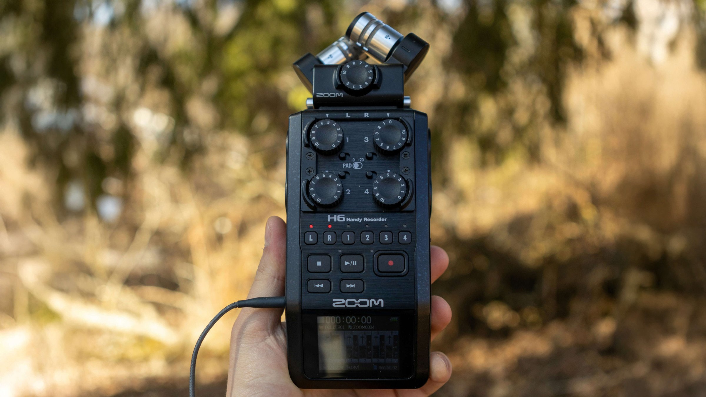 A portable audio recorder being held in front of a wooded area.