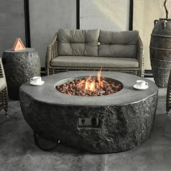 Round stone fire table with lit flames, outdoor setting with seating.