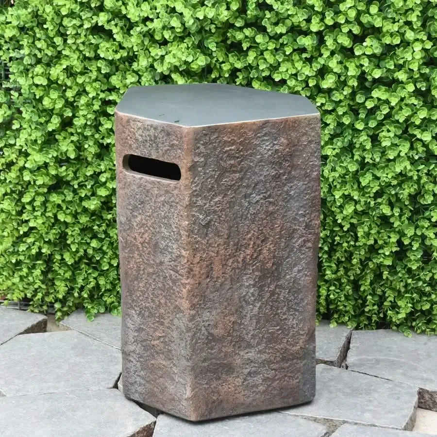 Elementi Columbia 15" Seat or Propane Tank Cover, a textured rectangular stool with a handle cutout, shown outdoors against a green foliage wall and stone pavers.