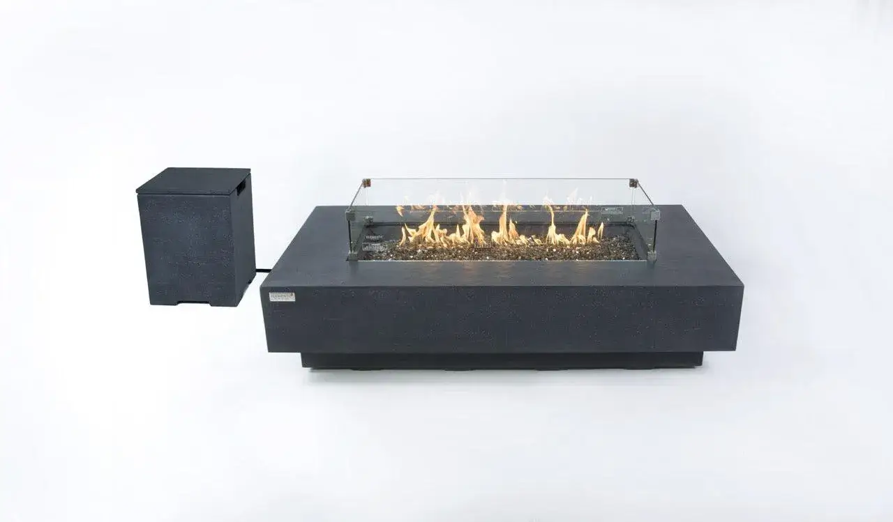 A dark grey rectangular fire table with a glass wind guard and lit flames, alongside a separate dark grey tank cover, on a white background.