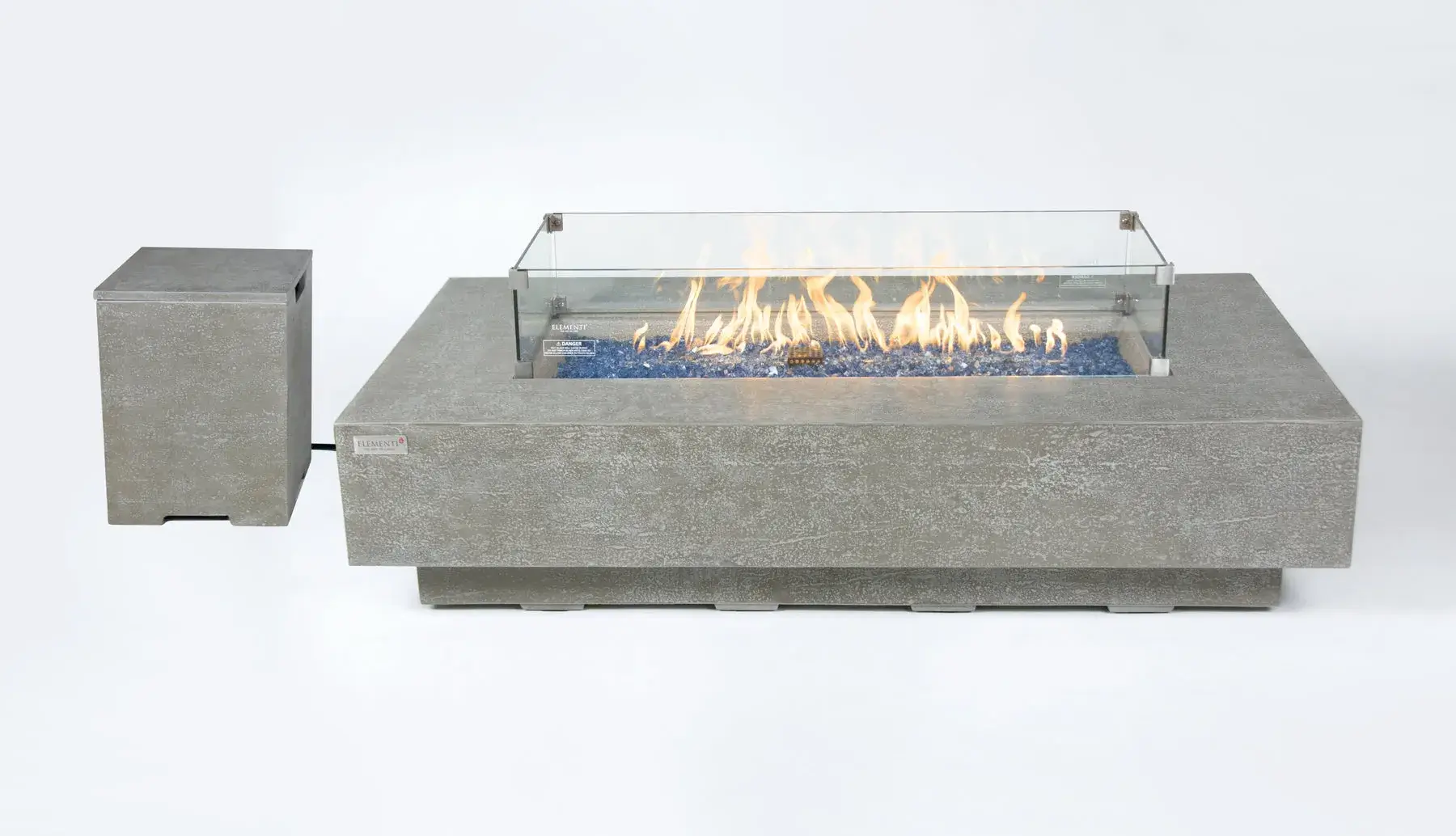 A light grey concrete rectangular fire table with a glass wind guard surrounding lit flames over blue glass fire beads. A matching light grey concrete tank cover is positioned to the left, all on a white background.