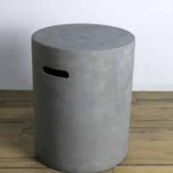A gas cylinder cover with a concrete look, possibly the Gas Cylinder Cover Elementi or Gardenforma gas cylinder cover, featuring a cylindrical shape and a handle cutout, shown indoors on a wooden floor.