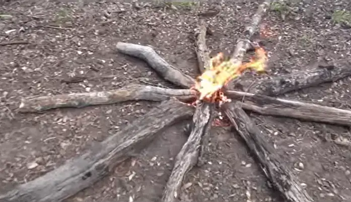 camp fire using star method. wood logs of various sizes are used with a kindle in the middle that has orange flames