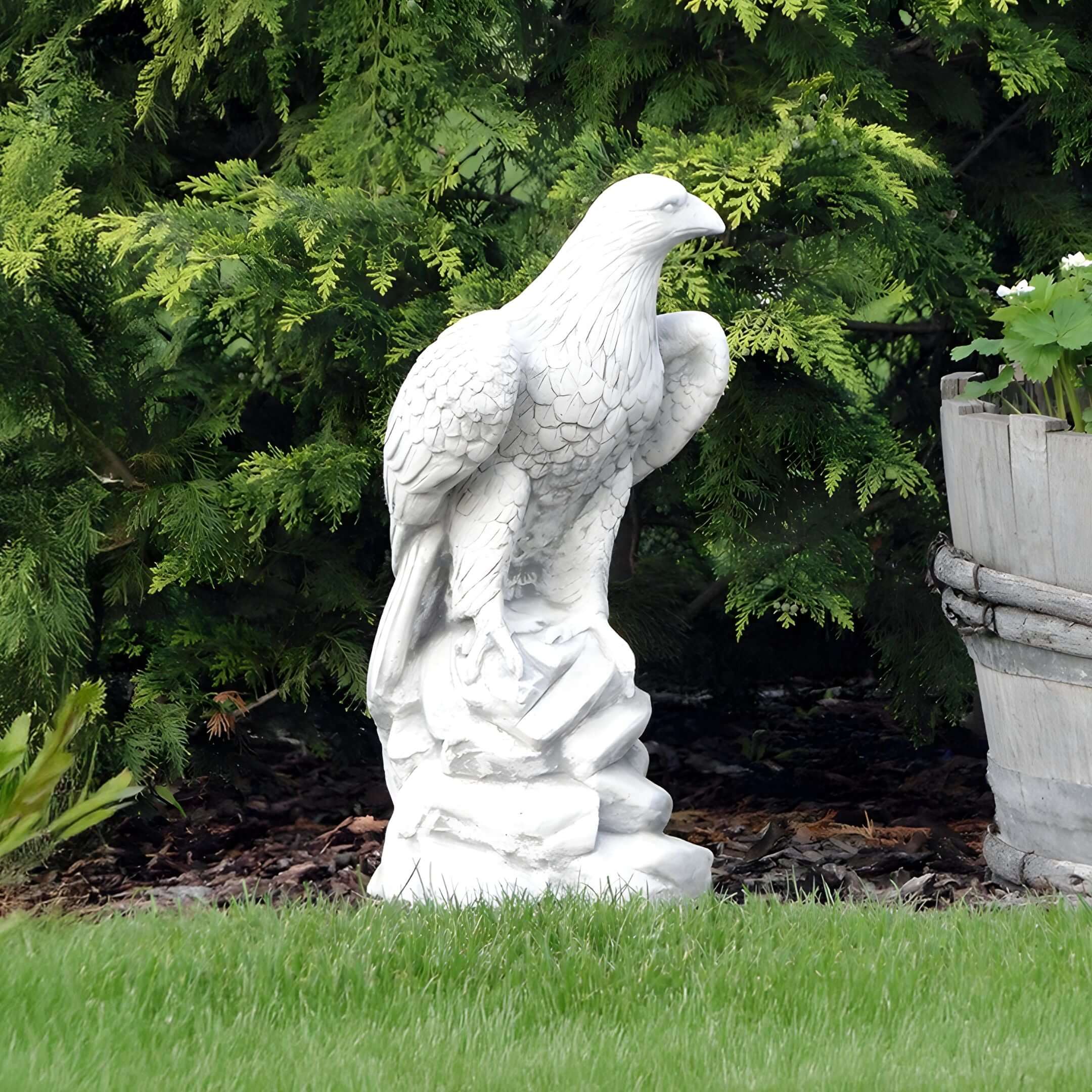 Eagle Sculpture in Garden – A detailed white eagle statue perched on a rock, surrounded by lush green foliage in a garden.