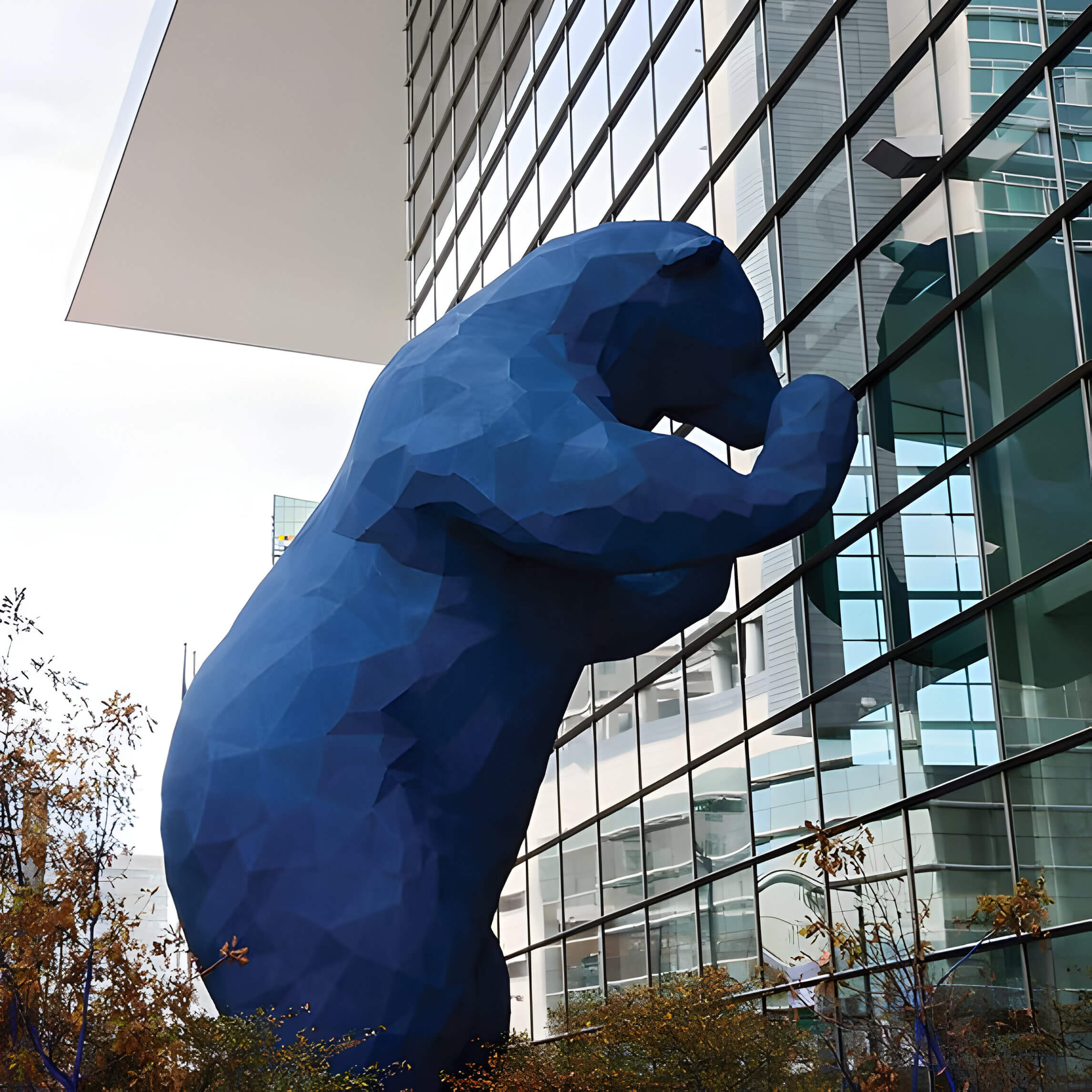 a large blue bear sculpture peering into a commercial building