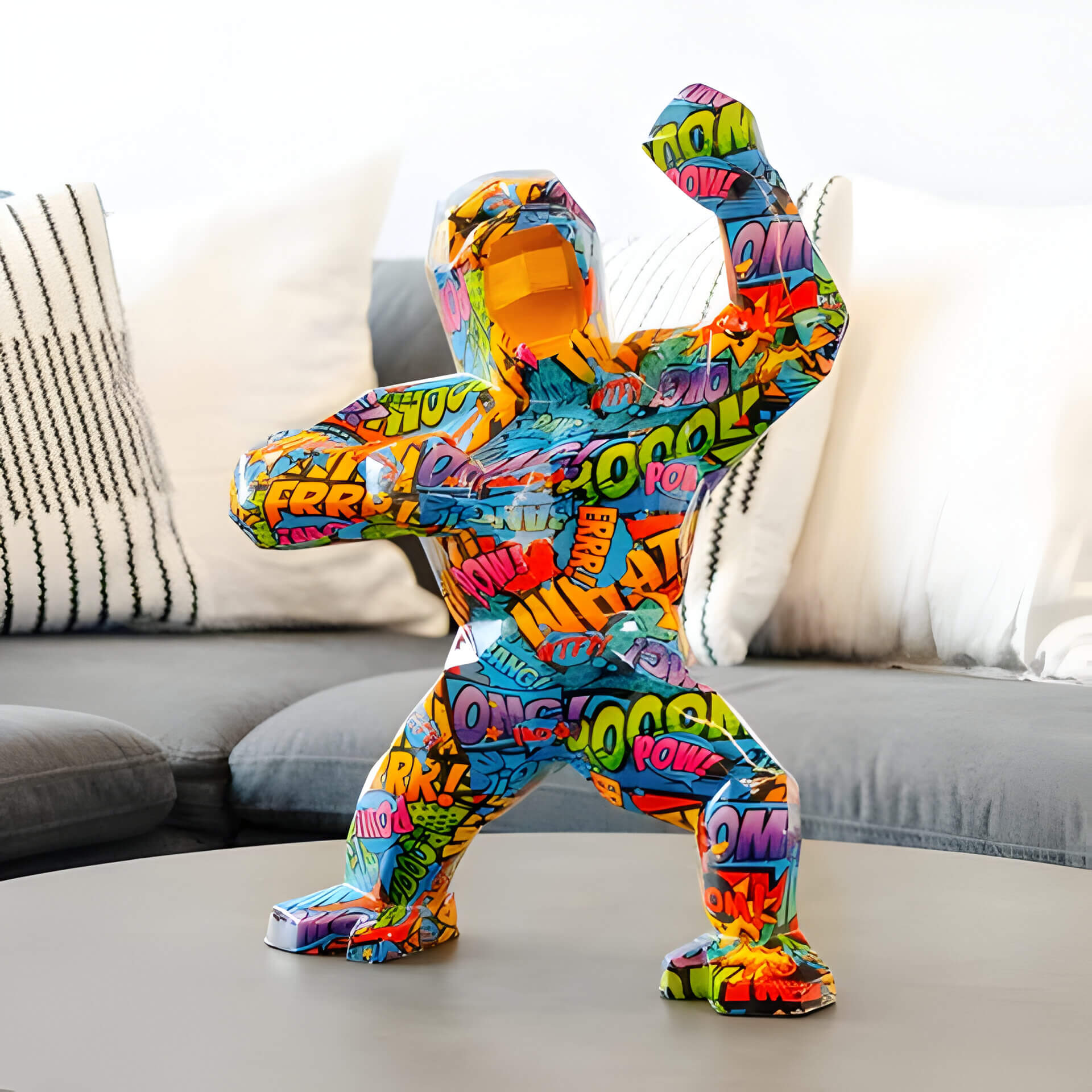 Vibrant geometric gorilla sculpture covered in comic-style text and graphics, posed with raised fists, placed on a coffee table in a modern living room.