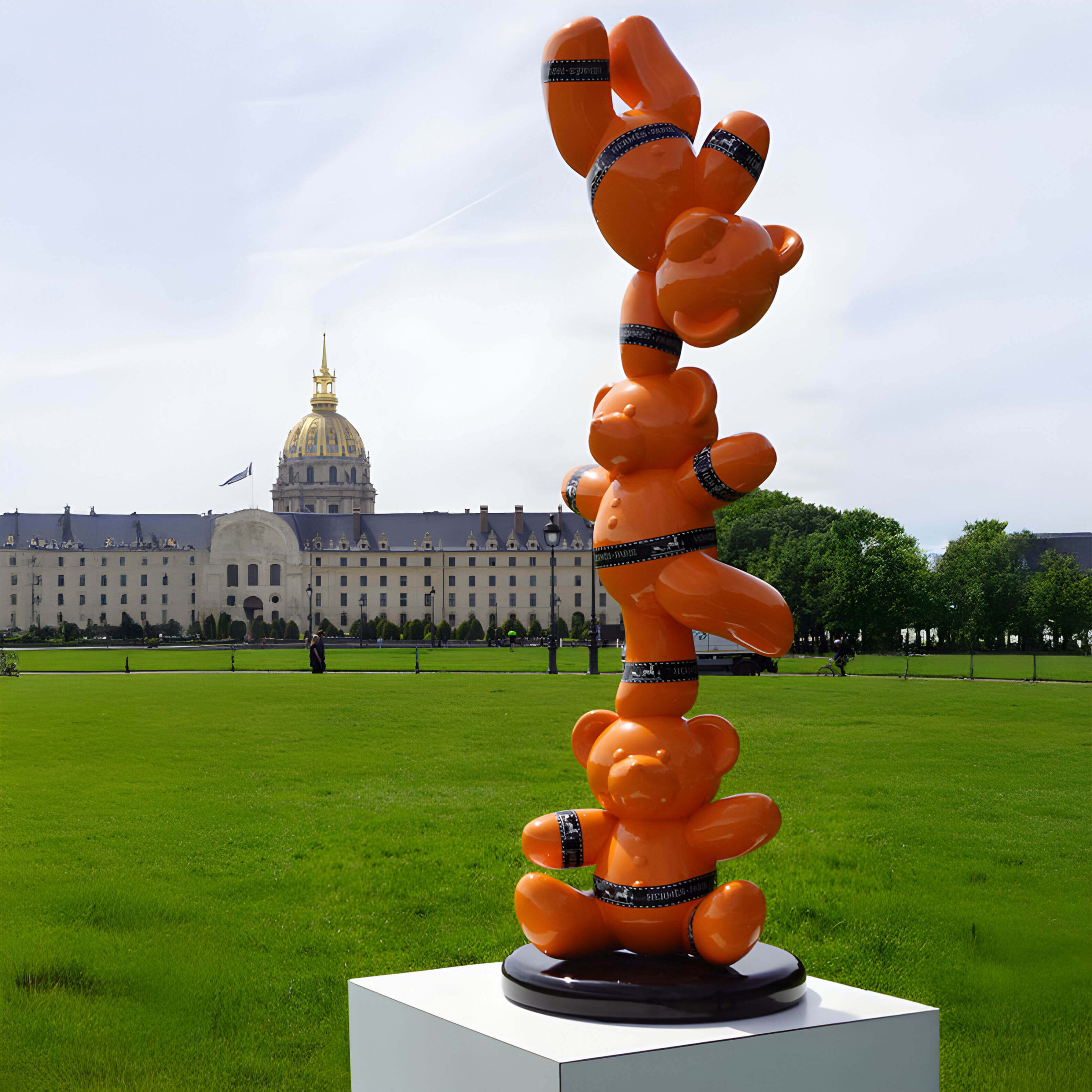 Stacked Orange Bear Sculpture – A playful tower of orange bear sculptures balancing in a public park with a grand historical building behind.