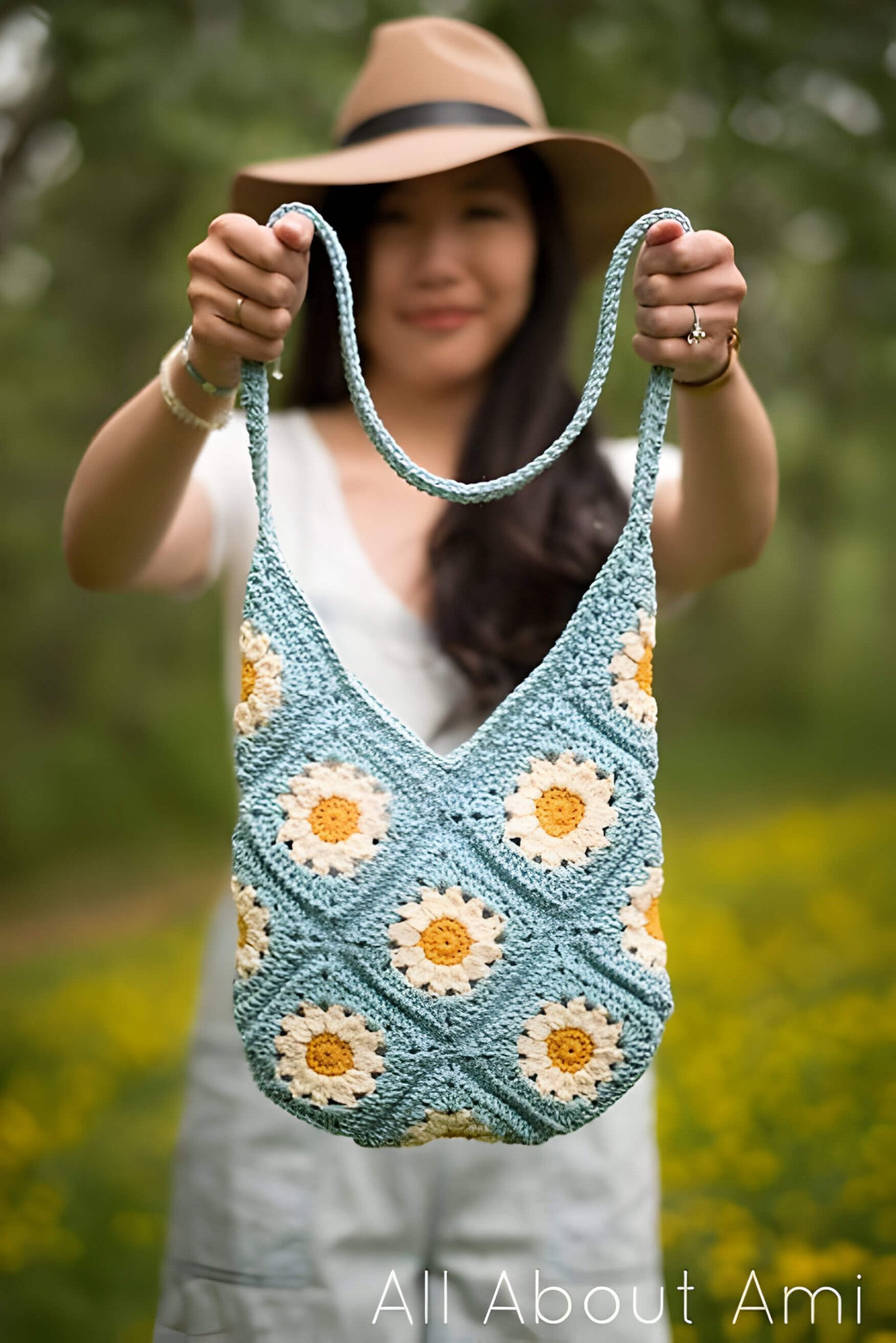 a lady in a brown hate and white t shirt holding a blue and white daisy crochet bag