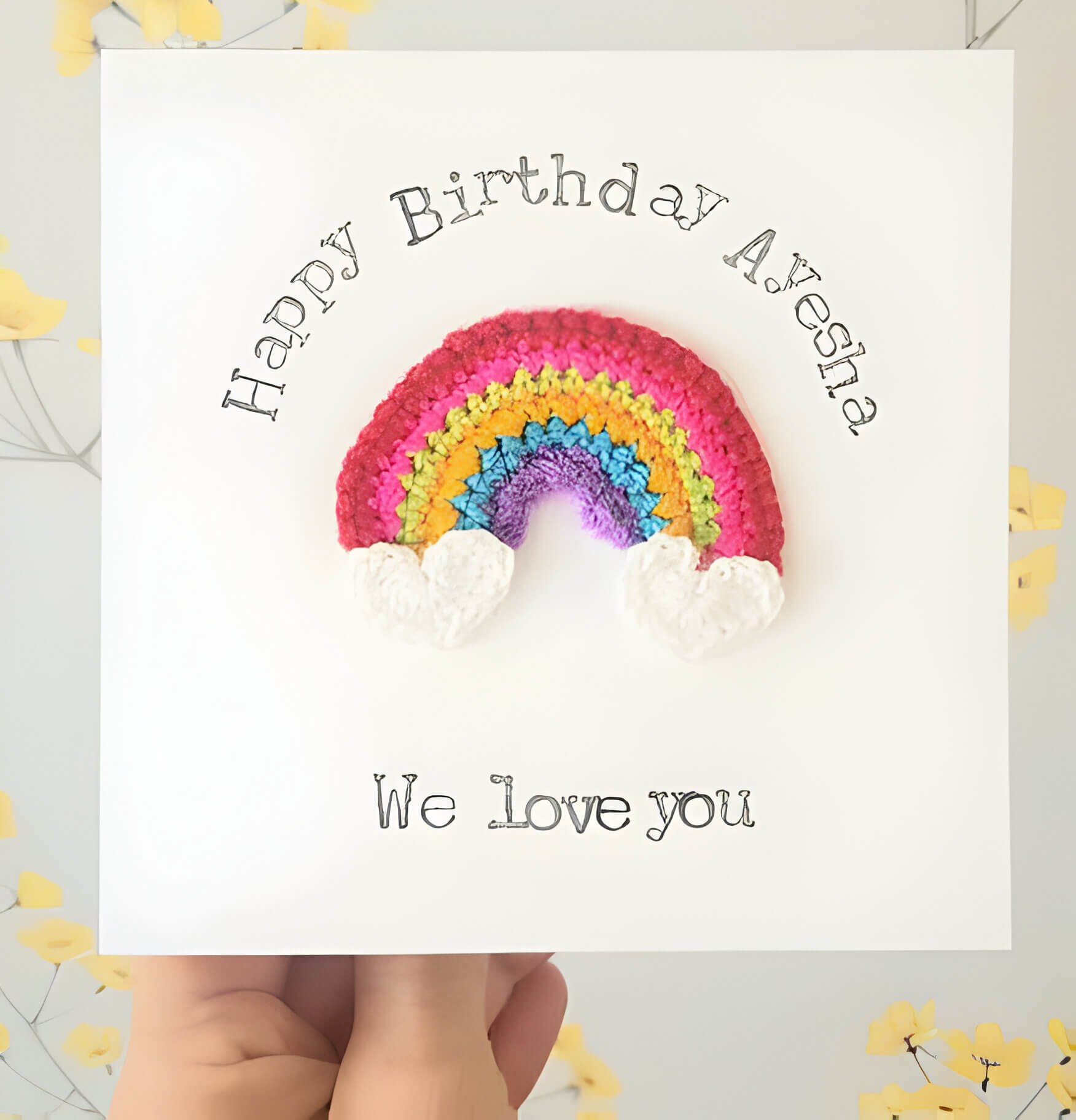 A white happy birthday card with a crochet rainbow
