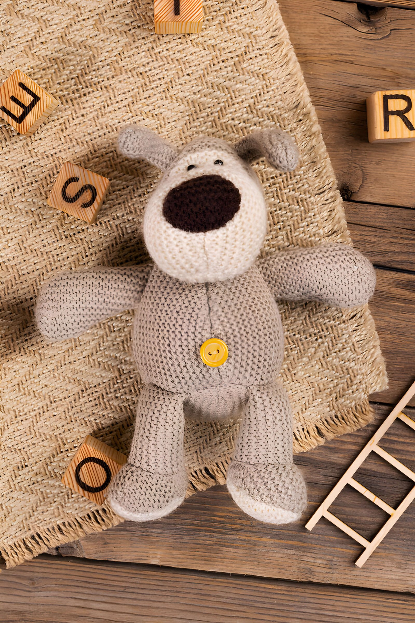 A brown crochet teddy on a table with wooden letters