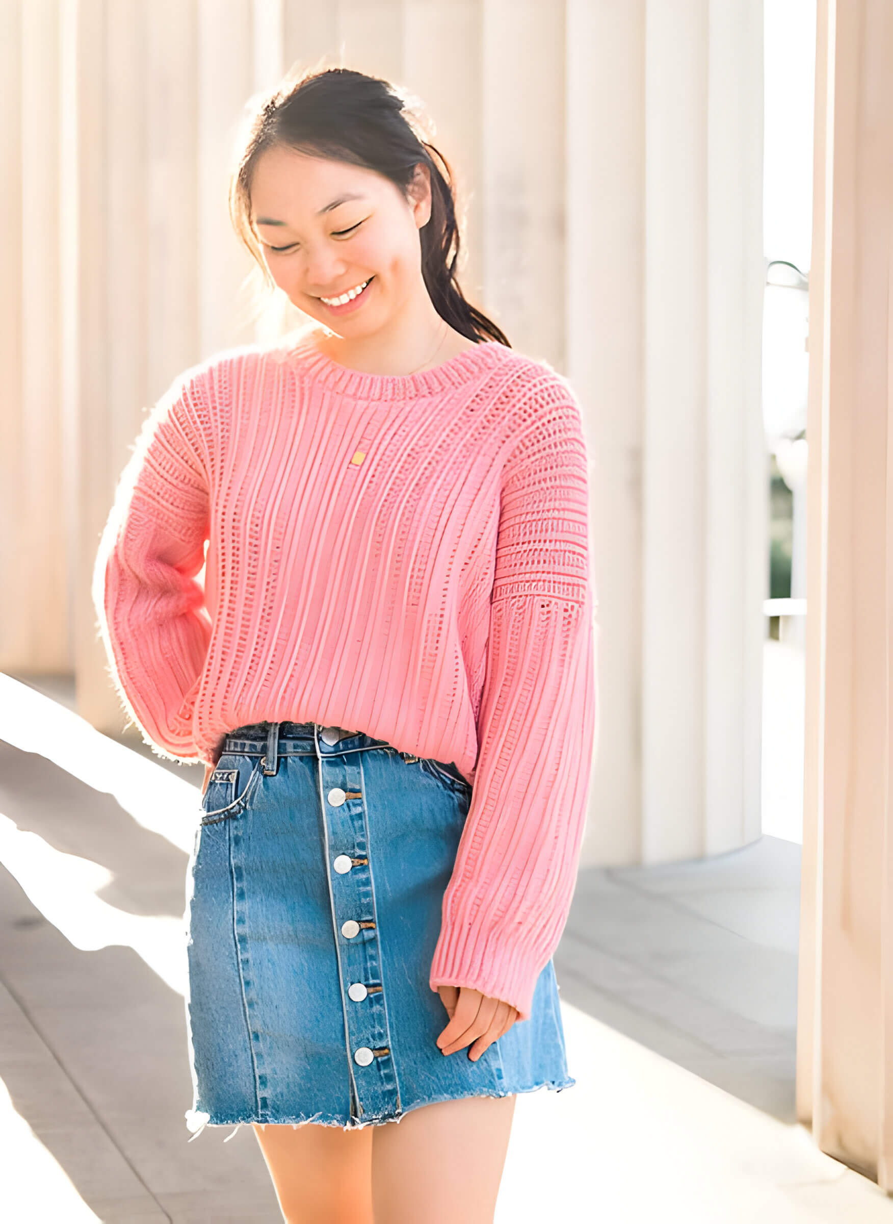 smiling woman wearing a pink crochet jumper and a denim skirt